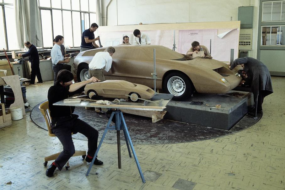 Это фото 1969 года скорее всего постановочное. Команда дизайнеров работает над полнорамерным макетом C111, довольно близким к реальному концепту, а на переднем плане — один из промежуточных макетов в масштабе 1:5. Объяснить, почему это делается параллельно, довольно сложно.